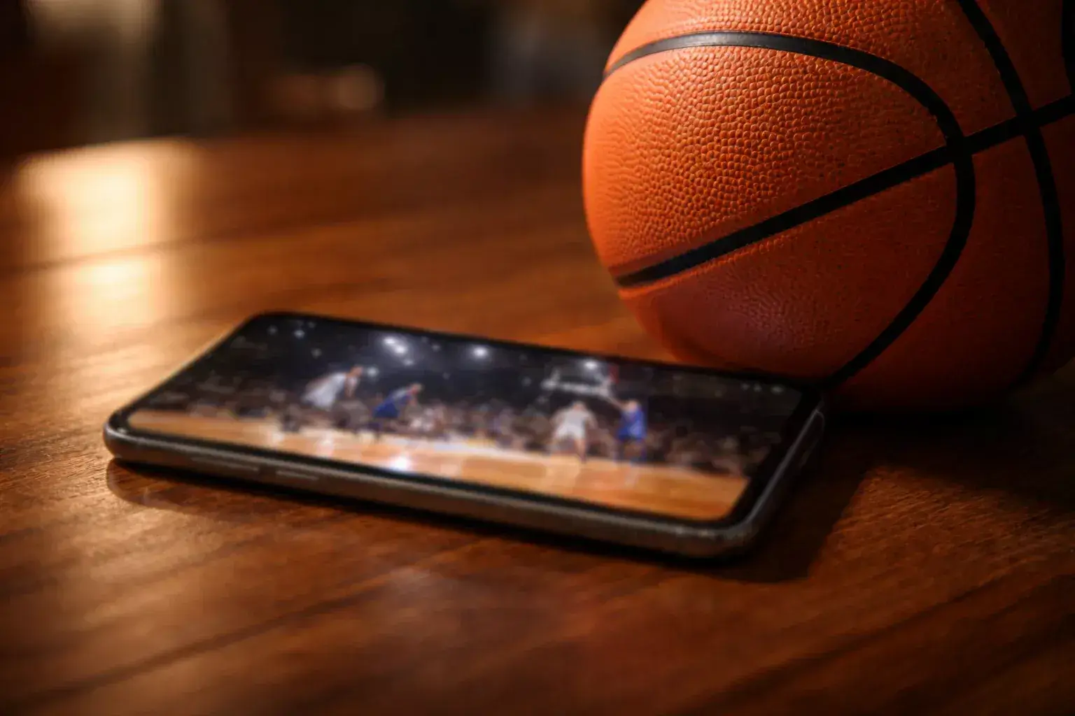 Smartphone con una partita di basket sullo schermo appoggiato accanto a un pallone