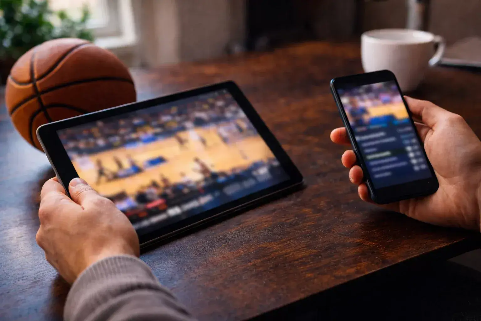 Persona che confronta diverse app di scommesse sul basket su un tablet e uno smartphone alla scrivania