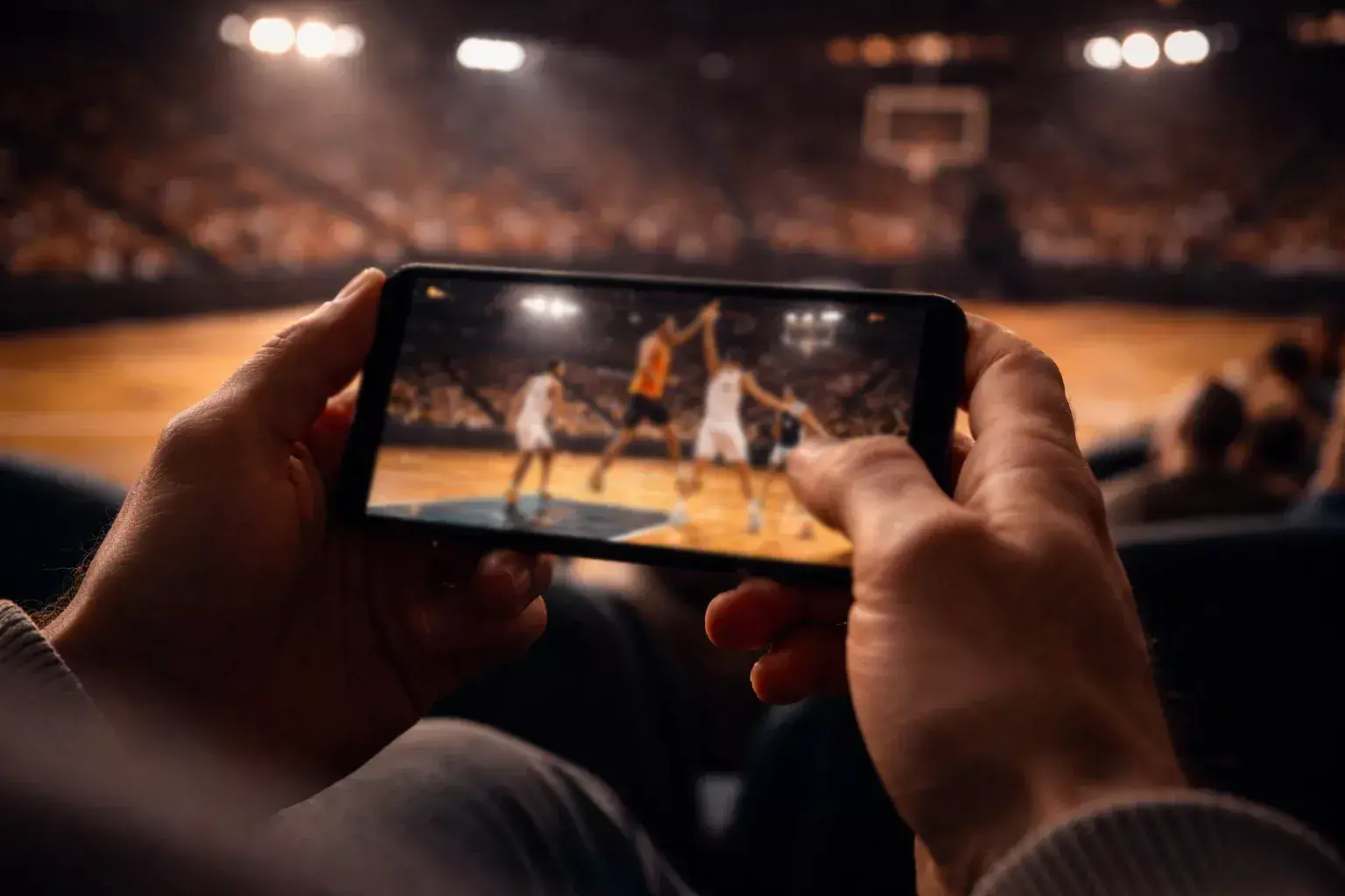 Tifoso che segue una partita di basket dal vivo sullo smartphone al palazzetto