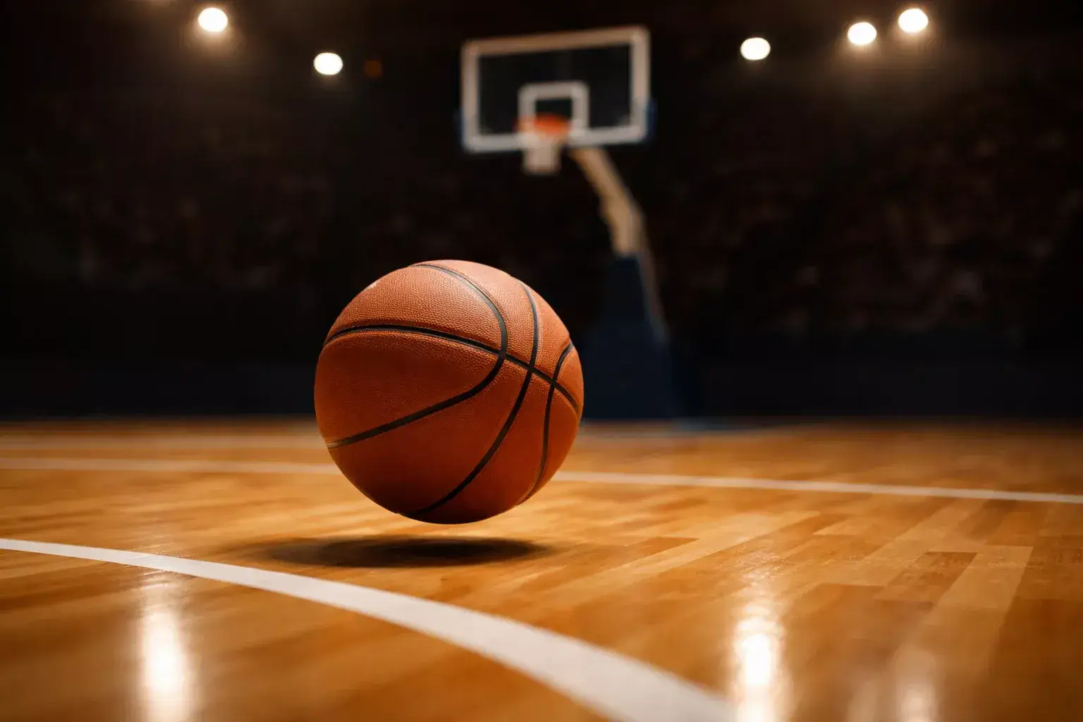 Pallone da basket che rimbalza sul parquet di un campo indoor con il tabellone segnapunti sullo sfondo